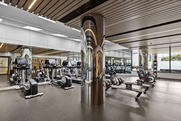 Une salle de sport moderne équipée de divers appareils d’exercice, notamment des tapis de course et des appareils de musculation, et dotée d’une grande colonne centrale.