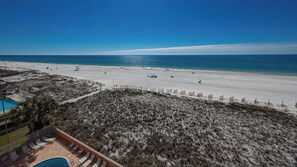 A beach view with a pool area, a fenced-off section, and a clear sky. - Seacrest 506- Relax, Unwind, and Enjoy (Gulf Shores)