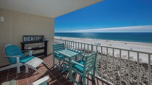 A balcony with a view of the beach, a chair, a table, and a sign that reads "BEACH".