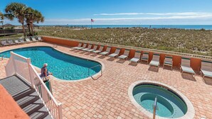 A pool area with a large pool, a smaller hot tub, and lounge chairs.