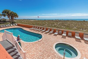 A pool area with a view of the ocean, a flag, and a person sitting by the pool. - Seacrest 506- Relax, Unwind, and Enjoy (Gulf Shores)