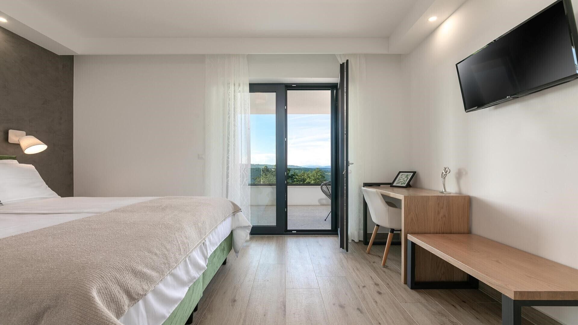 Une chambre d’hôtel moderne équipée d’un lit, d’un bureau, d’une banquette et d’un téléviseur fixé au mur.