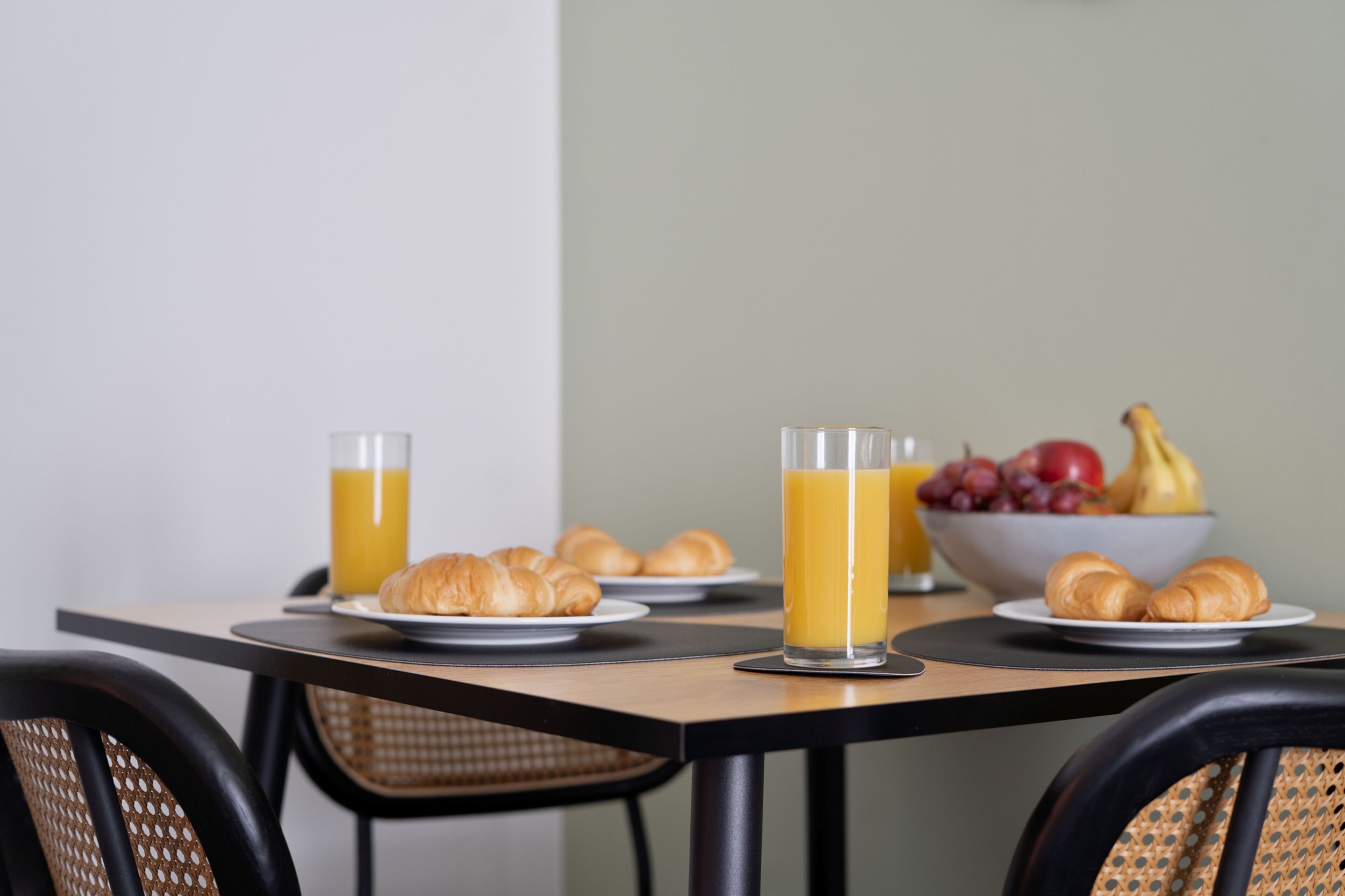 Una mesa de desayuno con croissants, zumo de naranja y un bol de fruta.