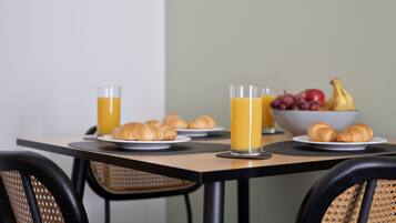 Una mesa de desayuno con croissants, zumo de naranja y un bol de fruta.