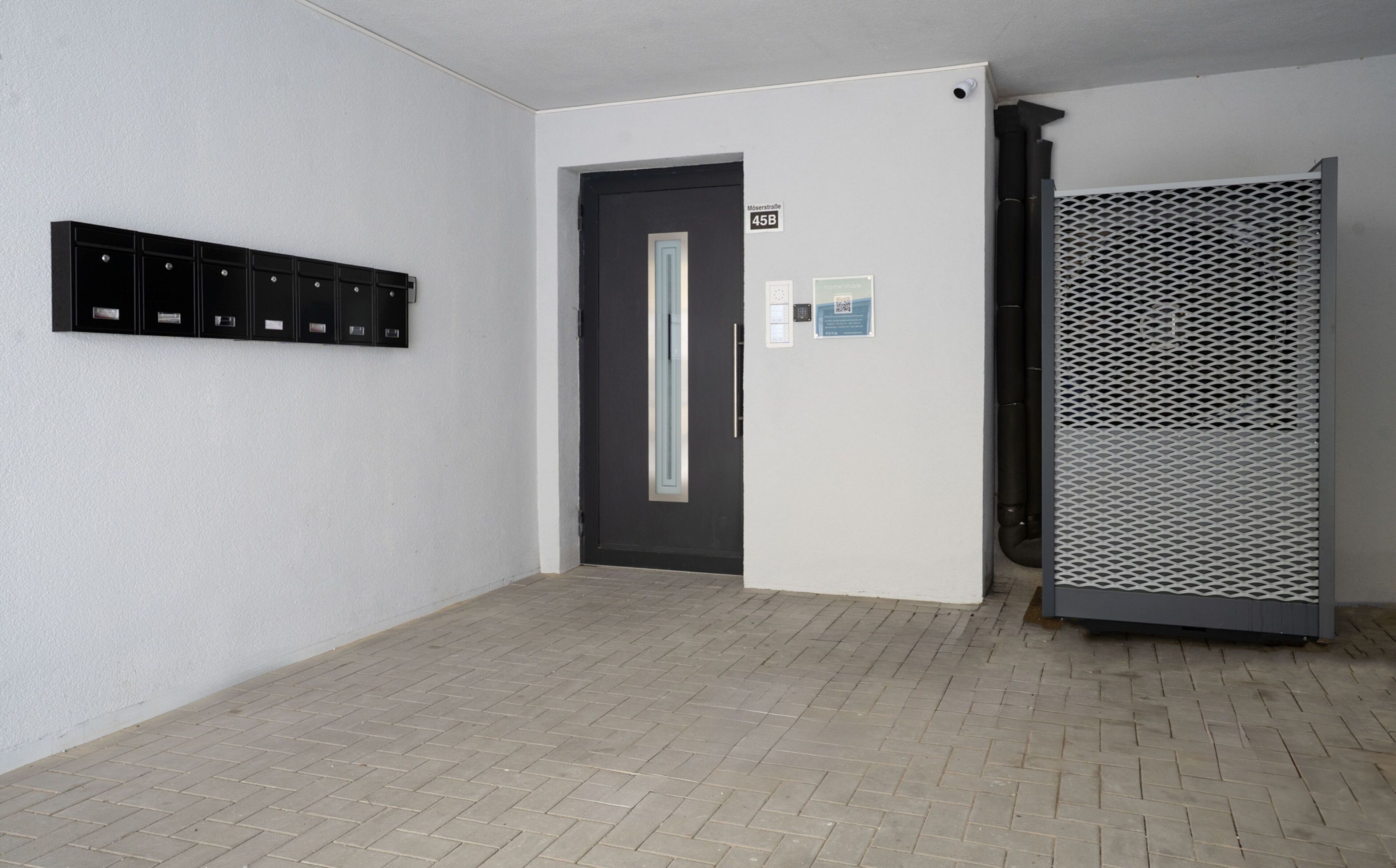 A hallway with a door, a mail slot, and a ventilation unit.
