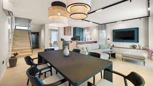 A modern living room with a dining area, a sofa set, and a TV mounted on the wall.