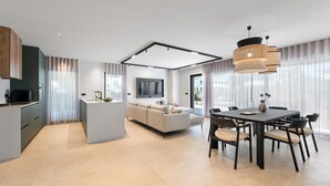 A modern kitchen with a built-in island, a dining area with a dark table and chairs, and a living area with a sofa and TV.