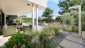 A modern outdoor pool area with lounge chairs, a covered seating area, and a view of the surrounding landscape.