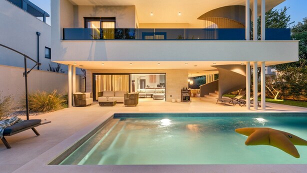 A modern two-story house with a swimming pool, outdoor seating, and a staircase leading to the upper floor.