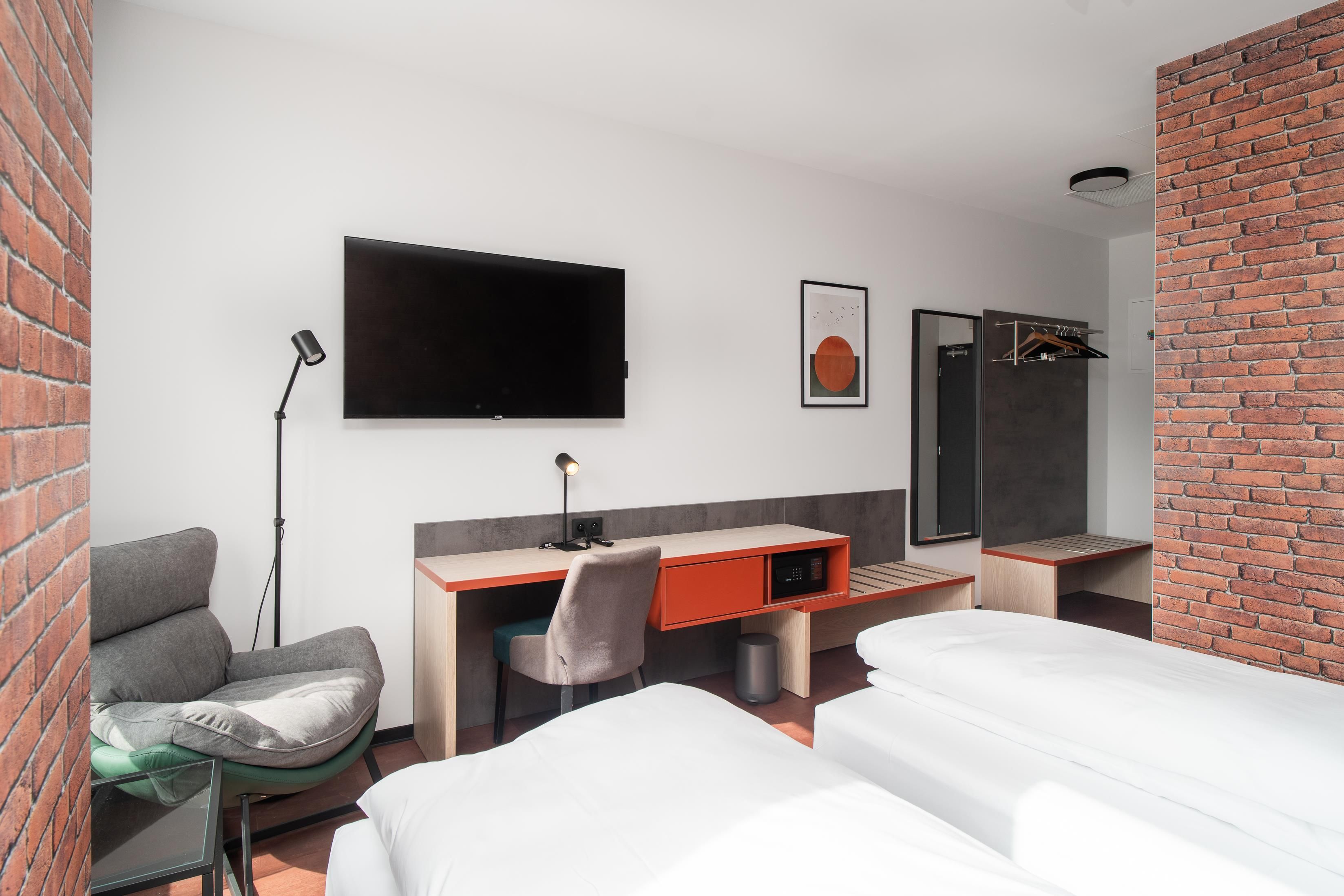 Una habitación de hotel moderna con una televisión de pantalla plana, un escritorio con una silla, una cama y una pared decorada con ladrillo.