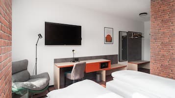 Una habitación de hotel moderna con una televisión de pantalla plana, un escritorio con una silla, una cama y una pared decorada con ladrillo.
