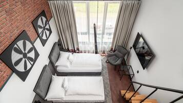Quarto de hotel moderno com duas camas, uma parede de tijolos, uma janela grande com cortinas, uma cadeira, uma escrivaninha e uma escada.