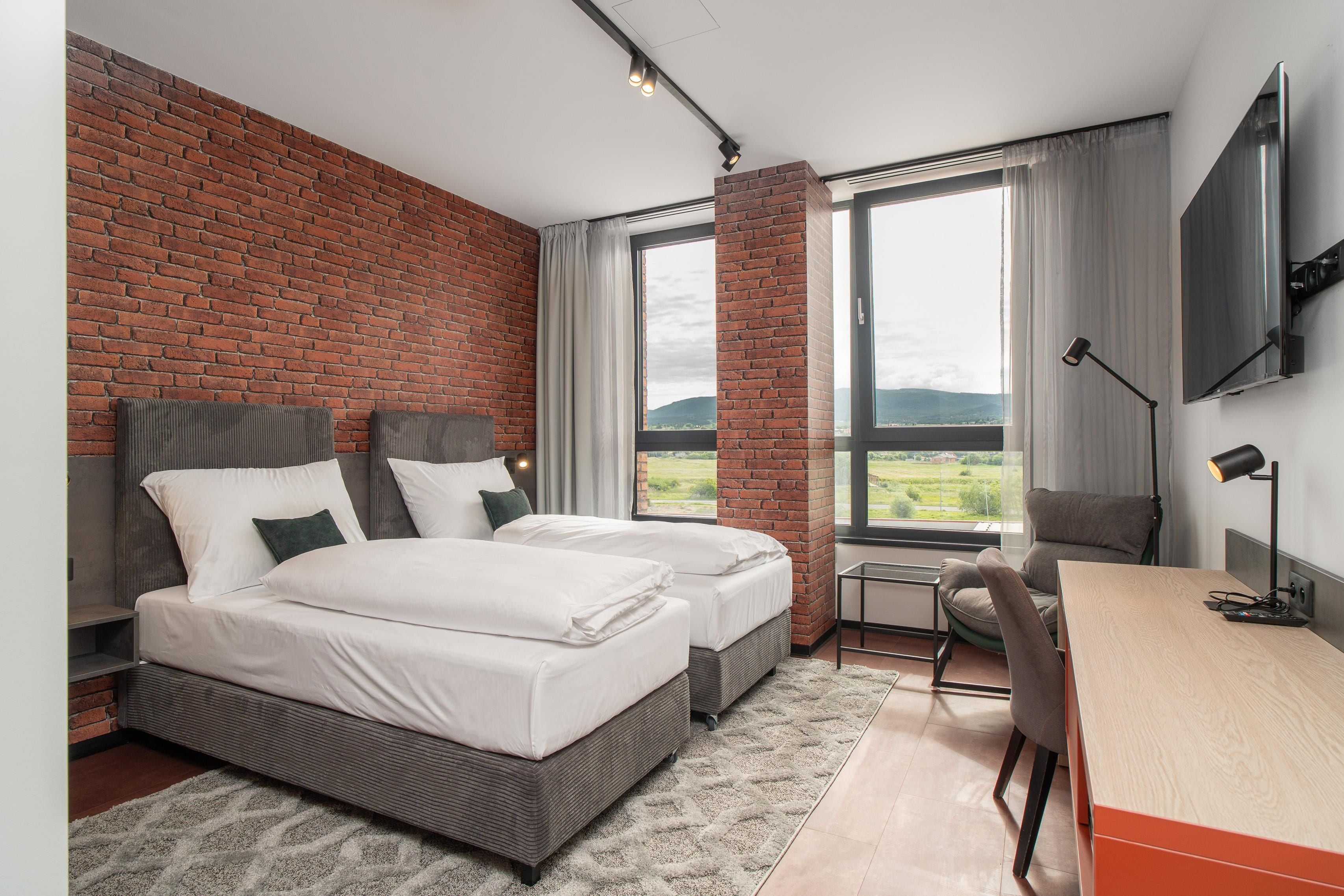 Moderni hotellihuone, jossa on kaksi sänkyä, työpöytä ja tuoli.