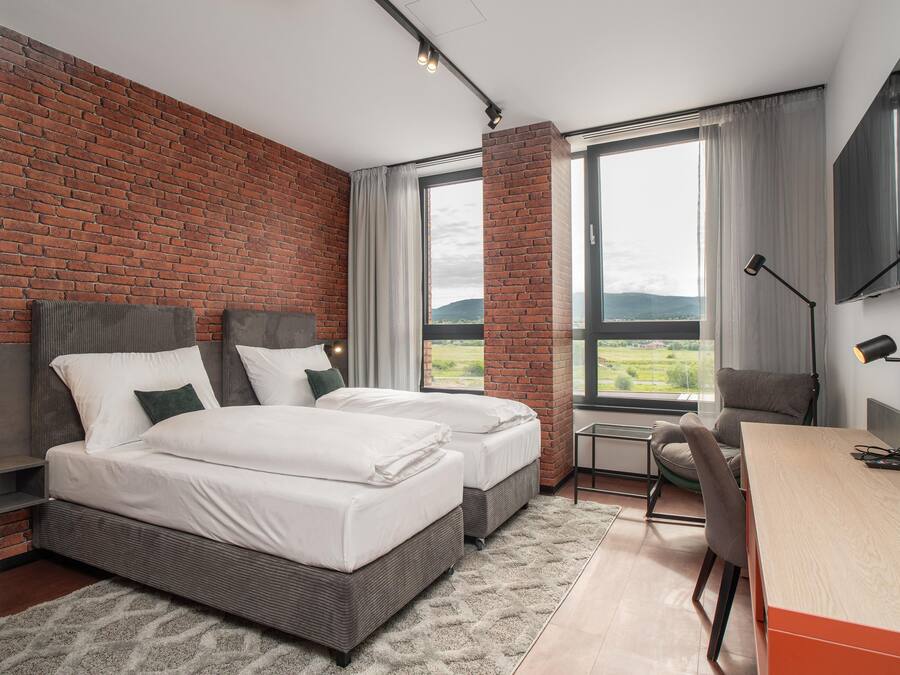 A modern hotel room with two beds, a desk, and a chair.