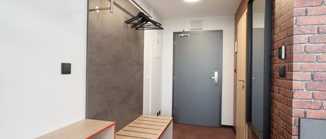 A hallway with a bench, a coat rack, a door, and a brick wall.