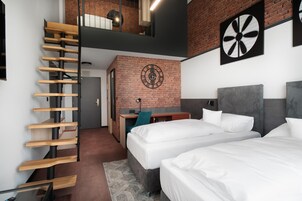 Una habitación de hotel moderna con escalera tipo loft, una pared de acento de ladrillo, un escritorio con silla y dos camas.