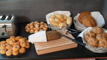Taula de buffet amb diferents tipus de pa i pastissos, una torradora i una taula de tallar.
