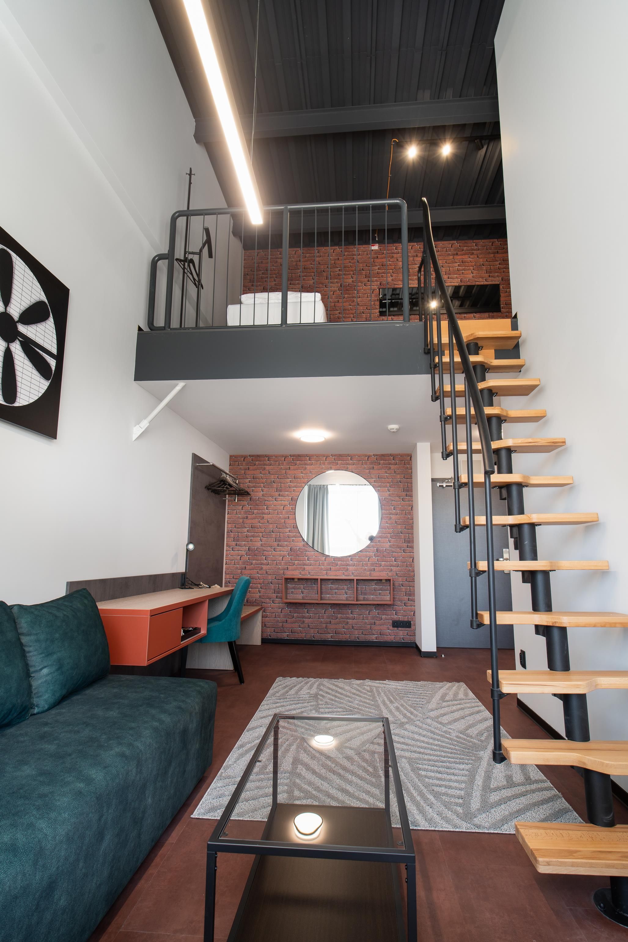 A modern loft apartment with a loft bed, a staircase, a desk, and a cozy seating area.