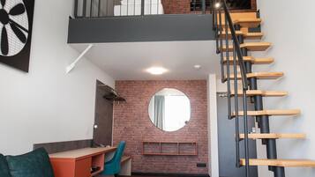 A modern loft apartment with a loft bed, a staircase, a desk, and a cozy seating area.