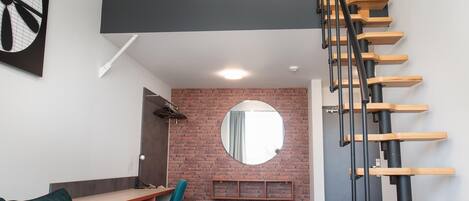 A modern loft apartment with a loft bed, a staircase, a desk, and a cozy seating area.