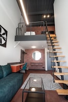 Un loft moderno con cama en altura, escalera, escritorio y un rincón de descanso acogedor.