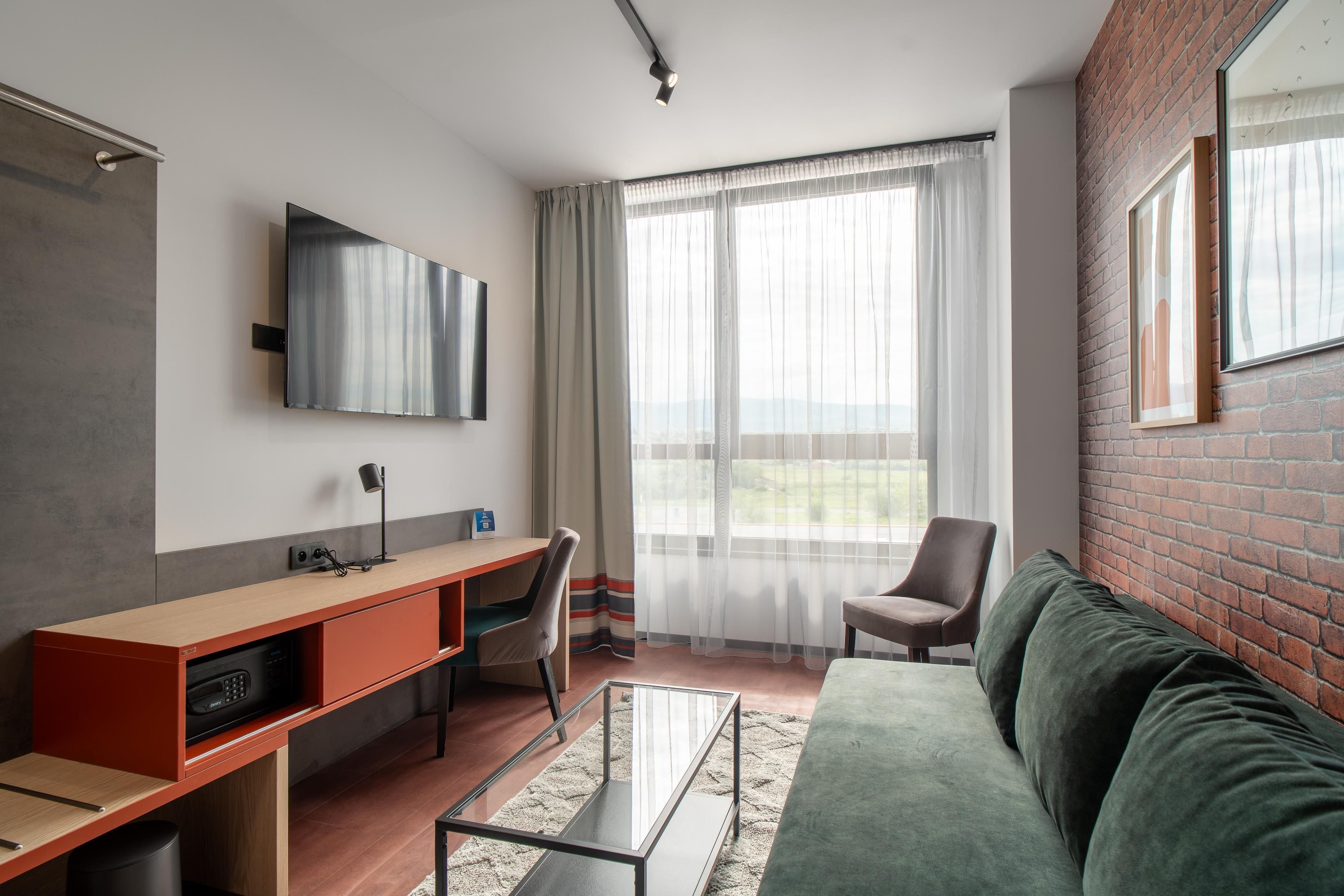 Una sala de estar moderna con un sofá, un escritorio, una silla y un televisor montado en la pared.