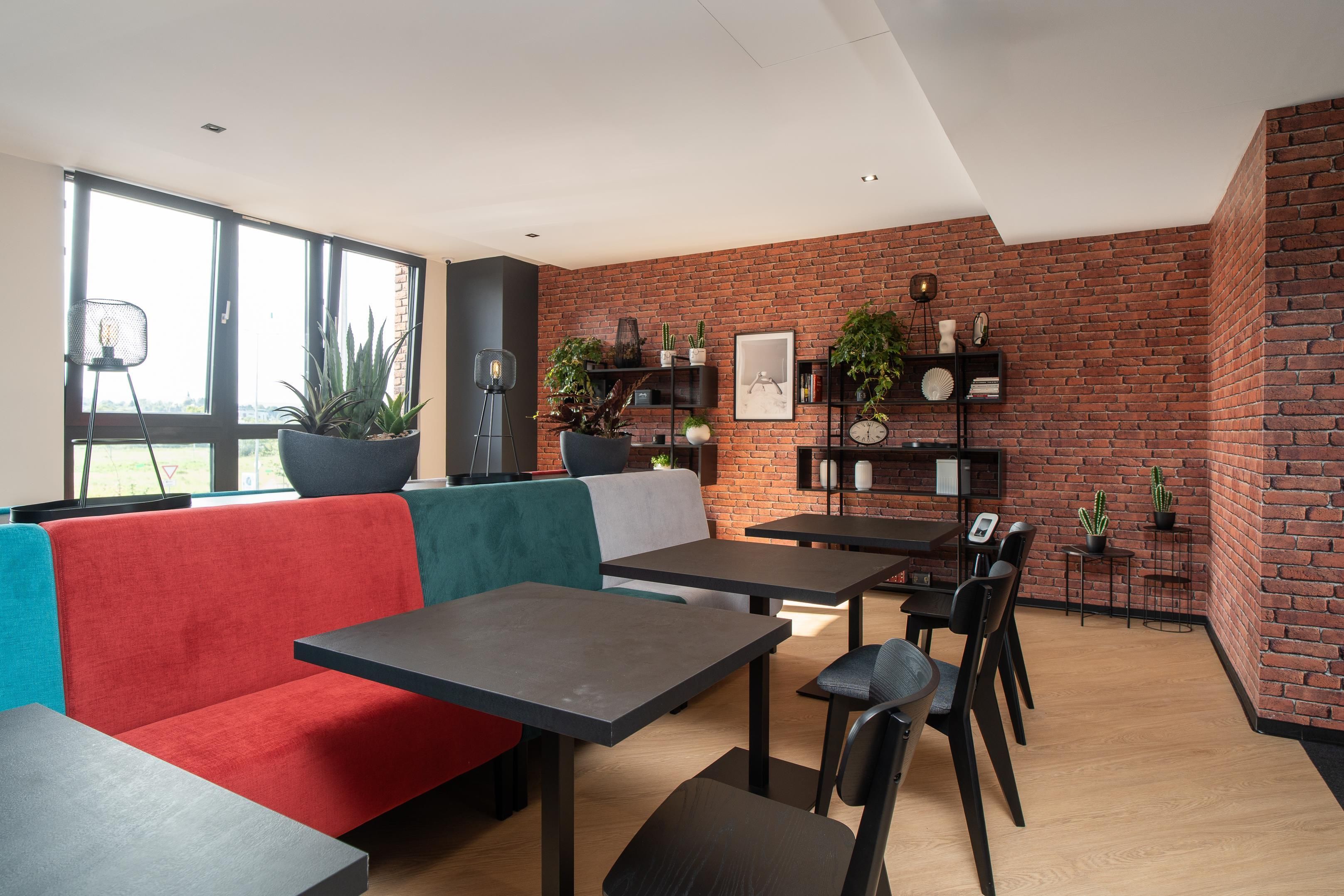 A modern interior with a brick wall, a red and teal sofa, and a dining area with tables and chairs.