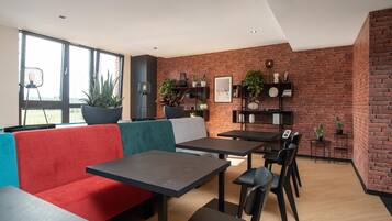 A modern interior with a brick wall, a red and teal sofa, and a dining area with tables and chairs.