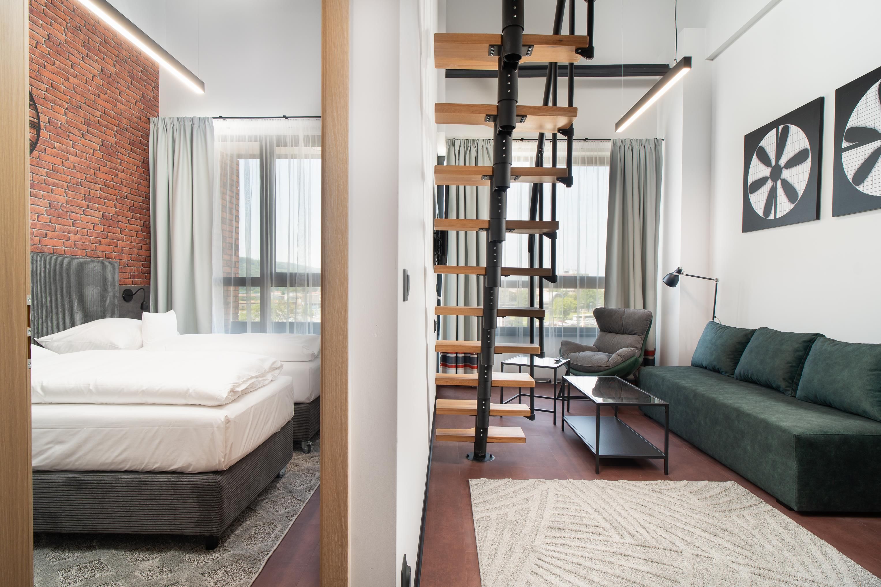 A modern hotel room with a bed, a sofa, a desk, and a staircase.