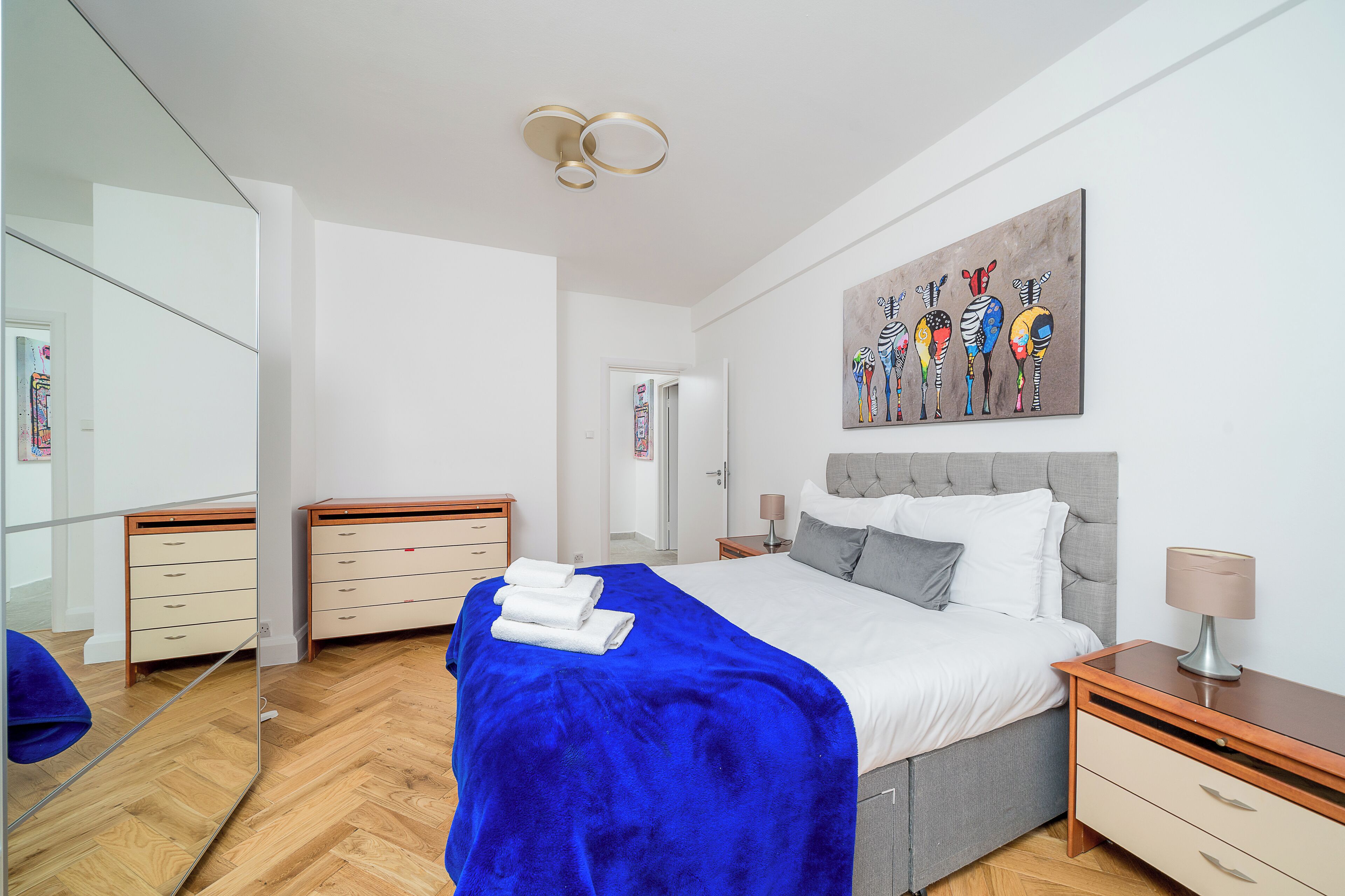 Un dormitorio moderno con una cama grande, una mesita de noche con lámpara, un espejo y una obra de arte en la pared.