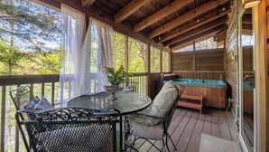 Een houten terras met een jacuzzi, een tafel met stoelen en uitzicht op bomen.