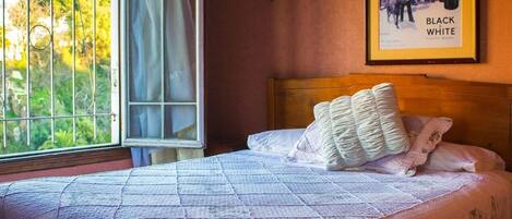 Un dormitorio con una cama grande, una ventana que da a zonas verdes y un cartel enmarcado en la pared.