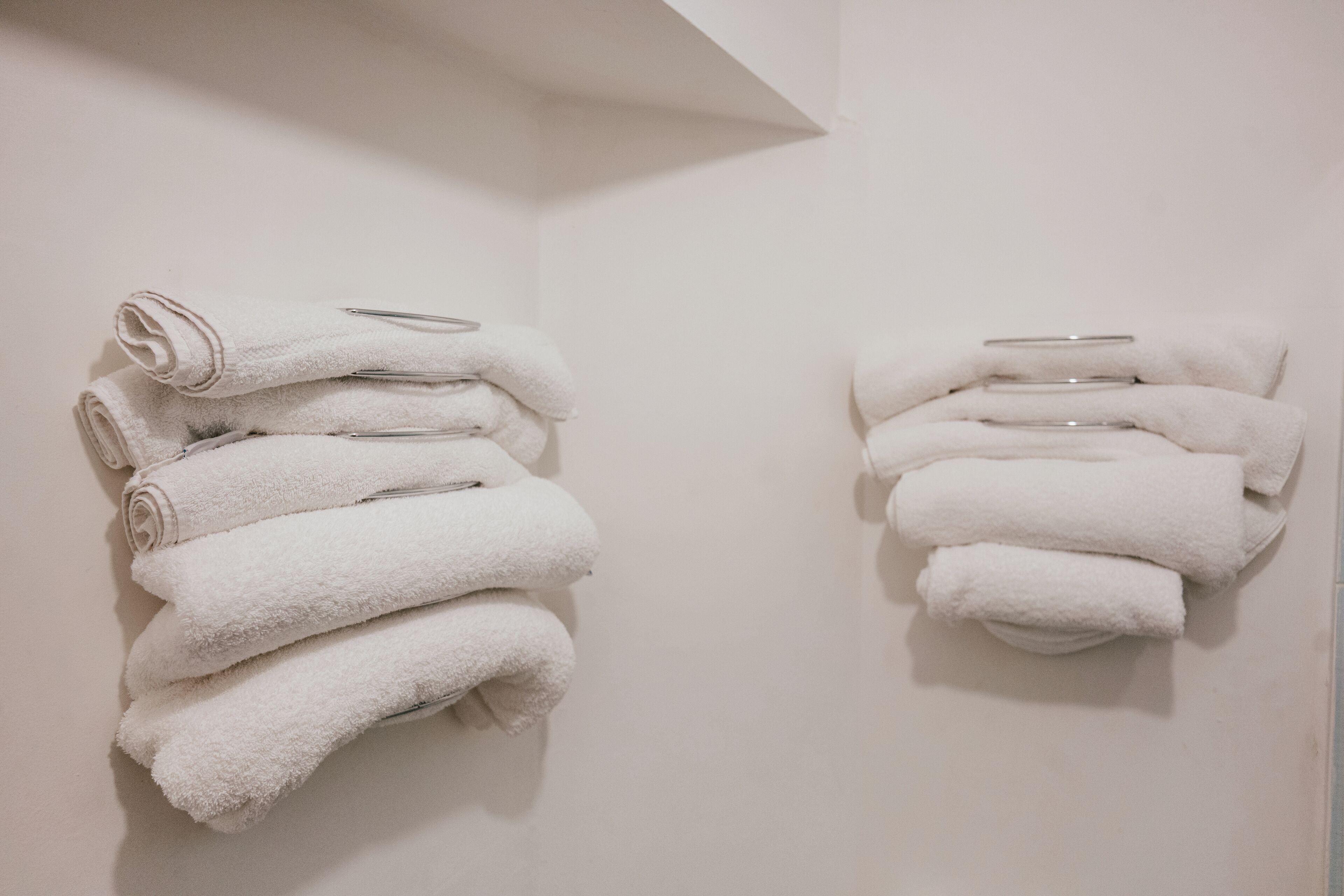 Two stacks of white towels on a wall, each with a metal bar.