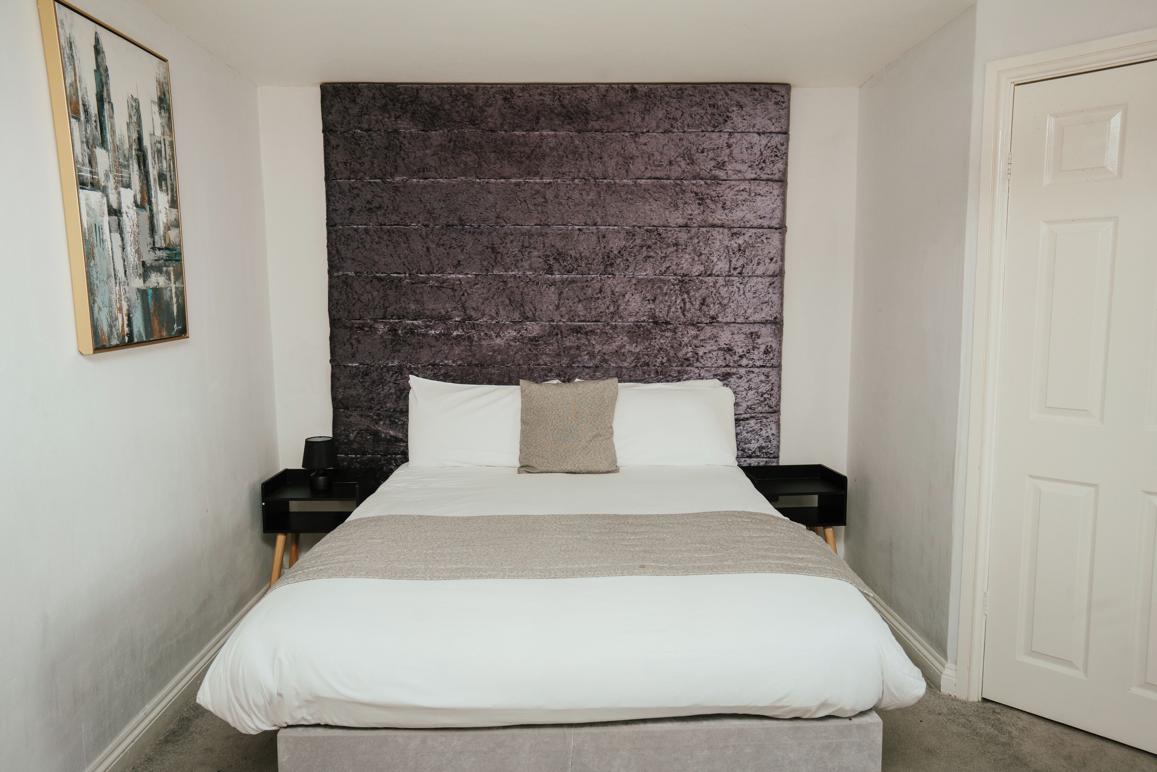 A bedroom with a large bed, a headboard with a textured design, a bedside table, and a door.