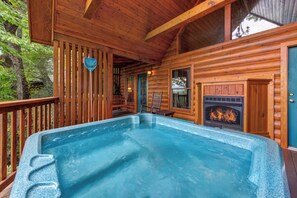 A wooden cabin with a hot tub, a fireplace, and a deck. - Cozy Cabin, Large Deck and Private Hot Tub (Sevierville)