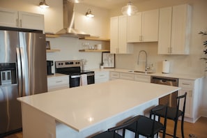 Una cocina moderna con armarios blancos, electrodomésticos de acero inoxidable y una isla central con taburetes de bar.