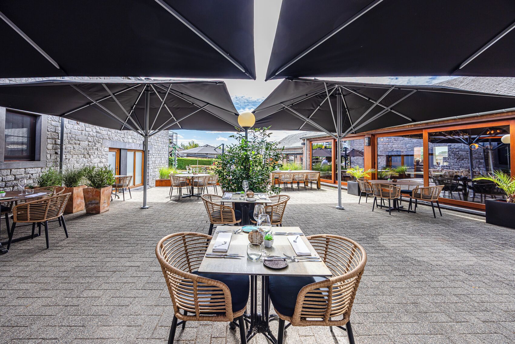 Une terrasse extérieure avec des tables et des chaises, des parasols et des plantes en pot.