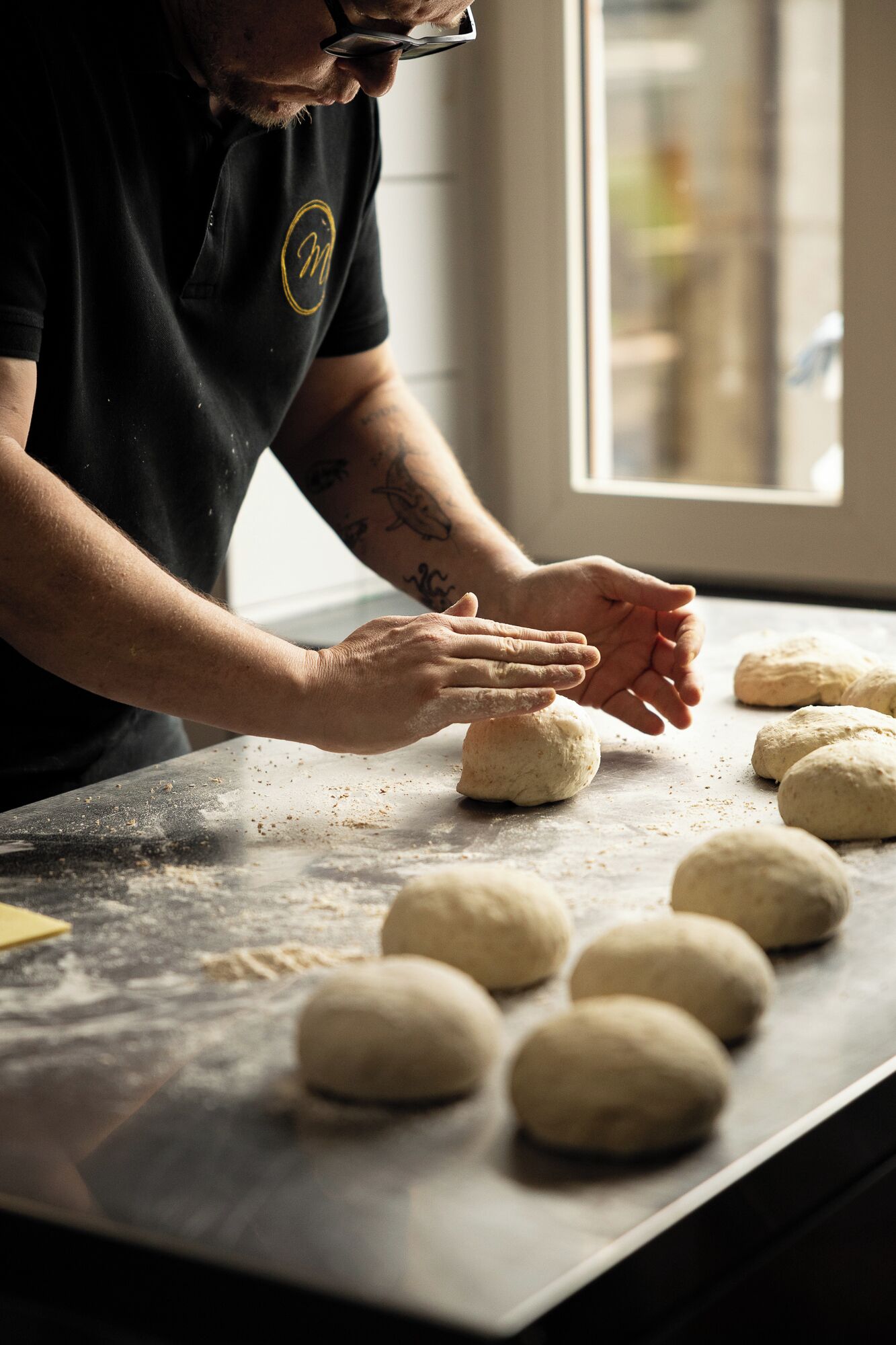 A person kneading dough on a floured surface with several dough balls.