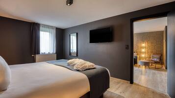 A modern hotel room with a large bed, a flat-screen TV, and a view of the hotel's lobby.