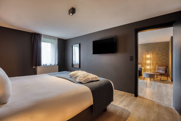 Une chambre d’hôtel moderne dotée d’un grand lit, d’un téléviseur à écran plat et offrant une vue sur le hall d’entrée de l’hôtel.