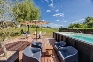 Terraza exterior con jacuzzi, zona de estar y una pérgola con sombrilla.