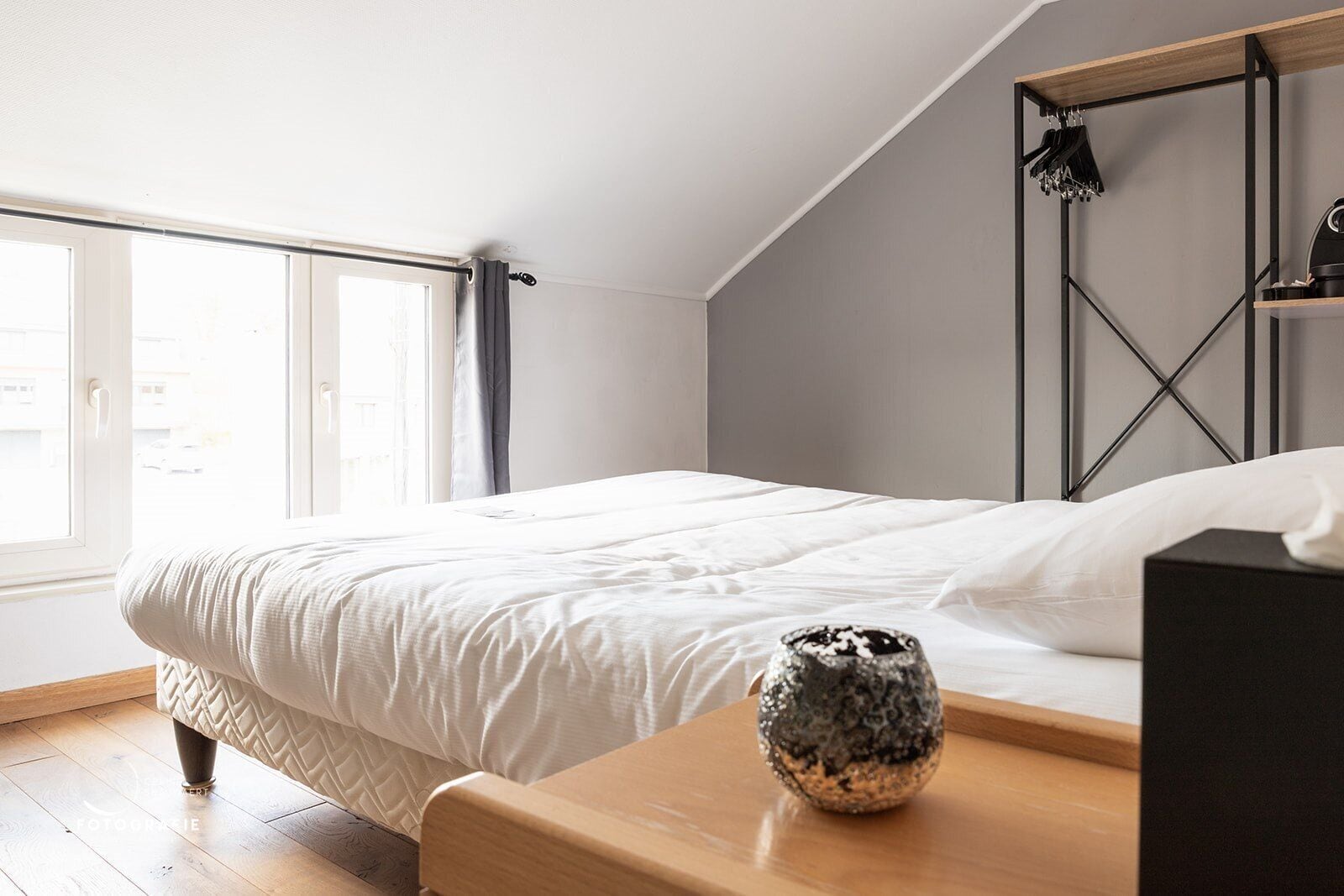 A bedroom with a bed, a wooden nightstand, a decorative vase, and a window with curtains.
