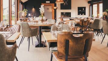 A restaurant with wooden tables and chairs, large windows, and a modern interior design.