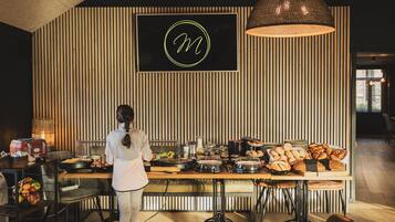 Montaje de buffet con diversos alimentos, una persona sirviendo y un letrero iluminado grande en la pared.