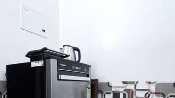 A compact refrigerator with a digital display, a kettle on top, and a small shelf.
