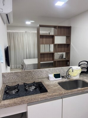 Una cocina con encimera de granito, estufa a gas, pileta y estantería de madera.