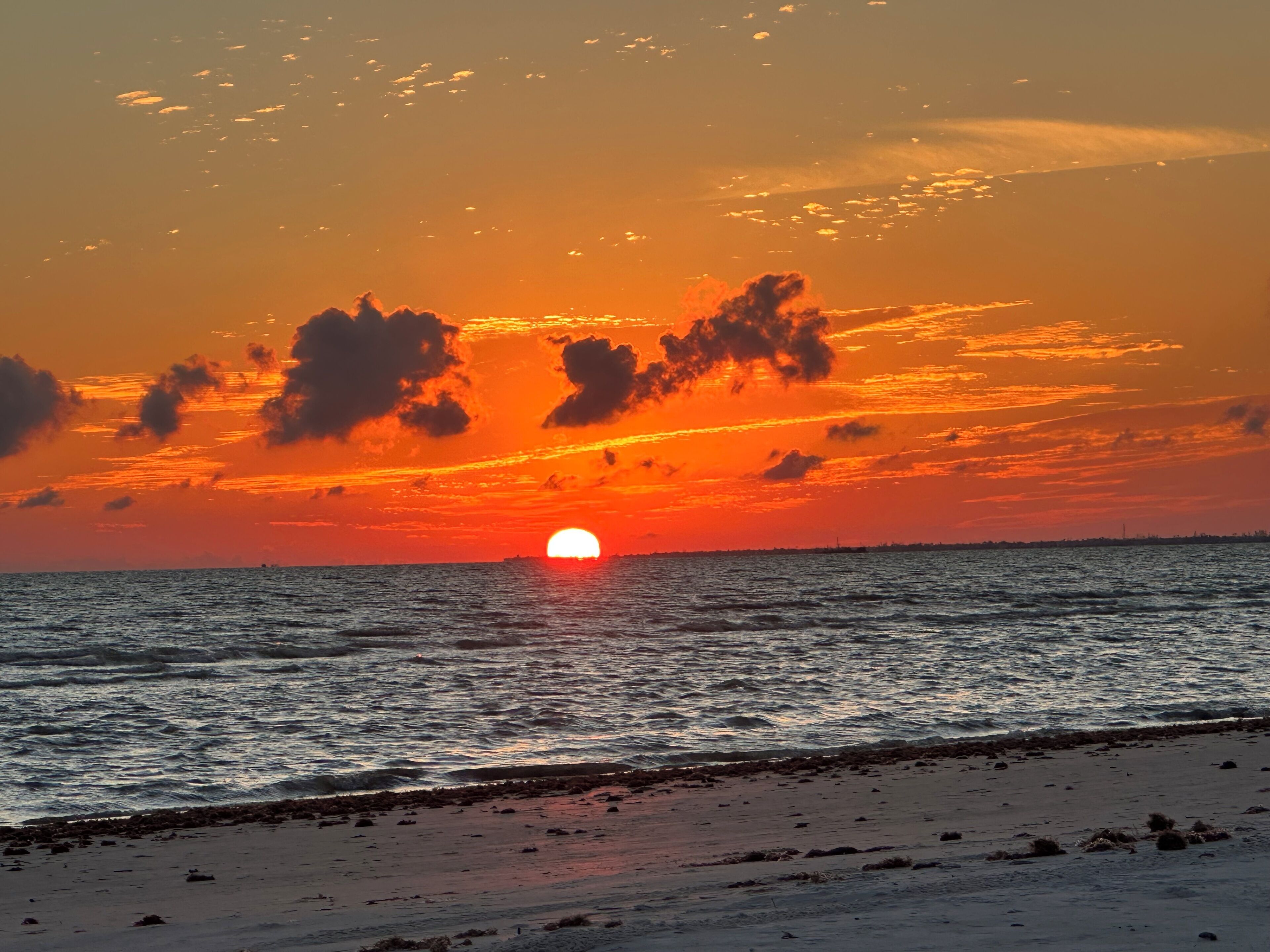A sunset over a beach with the sun partially visible above the horizon.