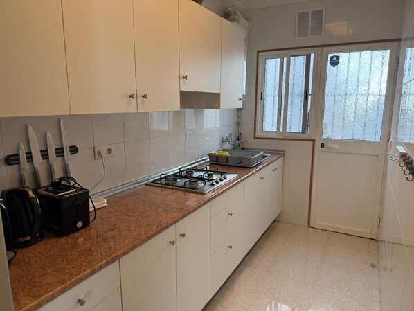 Une cuisine avec des meubles blancs, une cuisinière à gaz, un évier et une fenêtre en verre dépoli.