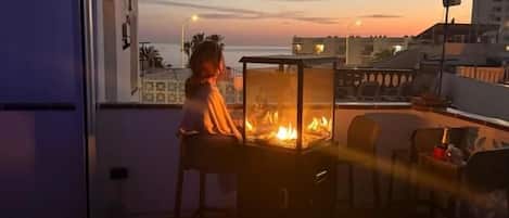 A balcony with a fire feature, outdoor seating, and a view of the sunset.