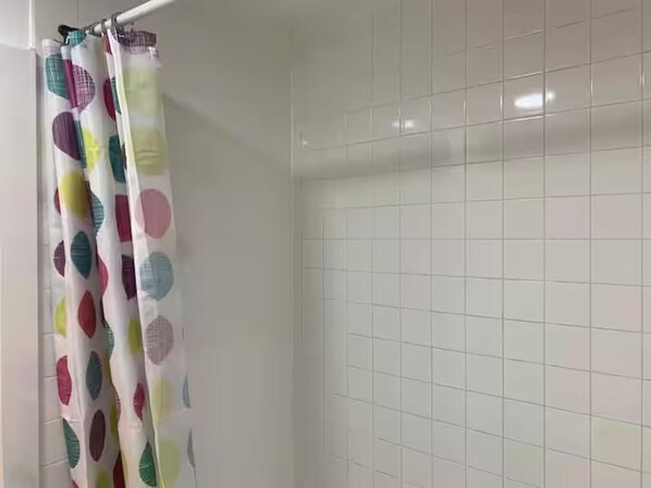 Ein Badezimmer mit weiß gefliesten Wänden und einer Duschtür mit einem farbenfrohen Blattmuster.